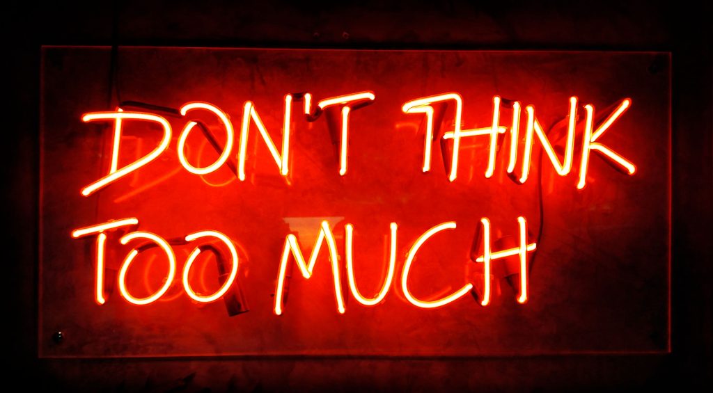 Illuminated neon sign showing DON'T THINK TO MUCH on black background